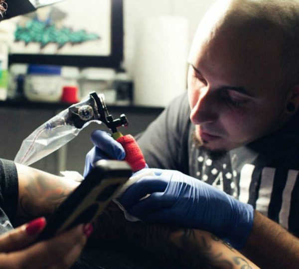 A tattoo artist working on a client's arm in a studio.