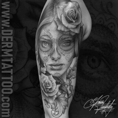Black and grey tattoo of a woman's face with floral and skull designs.