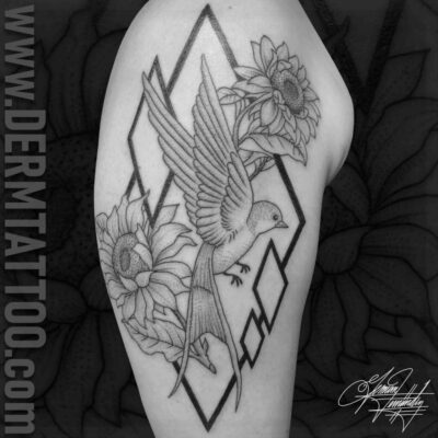 Black and gray tattoo of a hummingbird and flowers inside a geometric diamond frame.