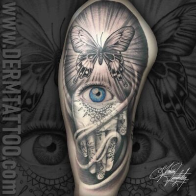 A surreal tattoo of a large blue eye with a moth above and skeletal elements below.