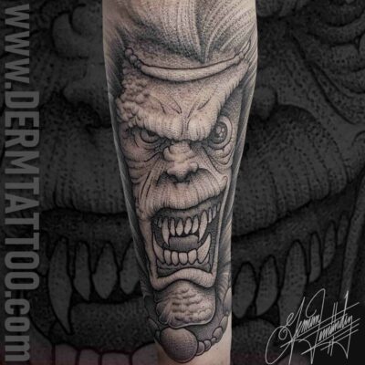 A detailed black and gray tattoo of a fierce, snarling face on a forearm.