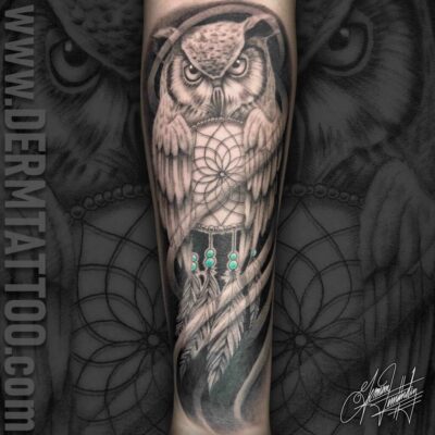 A detailed black and gray owl tattoo on a forearm.